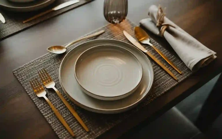 An elegant and modern table setting with layered plates, gold cutlery, and a simple napkin, ready for a dinner party.
