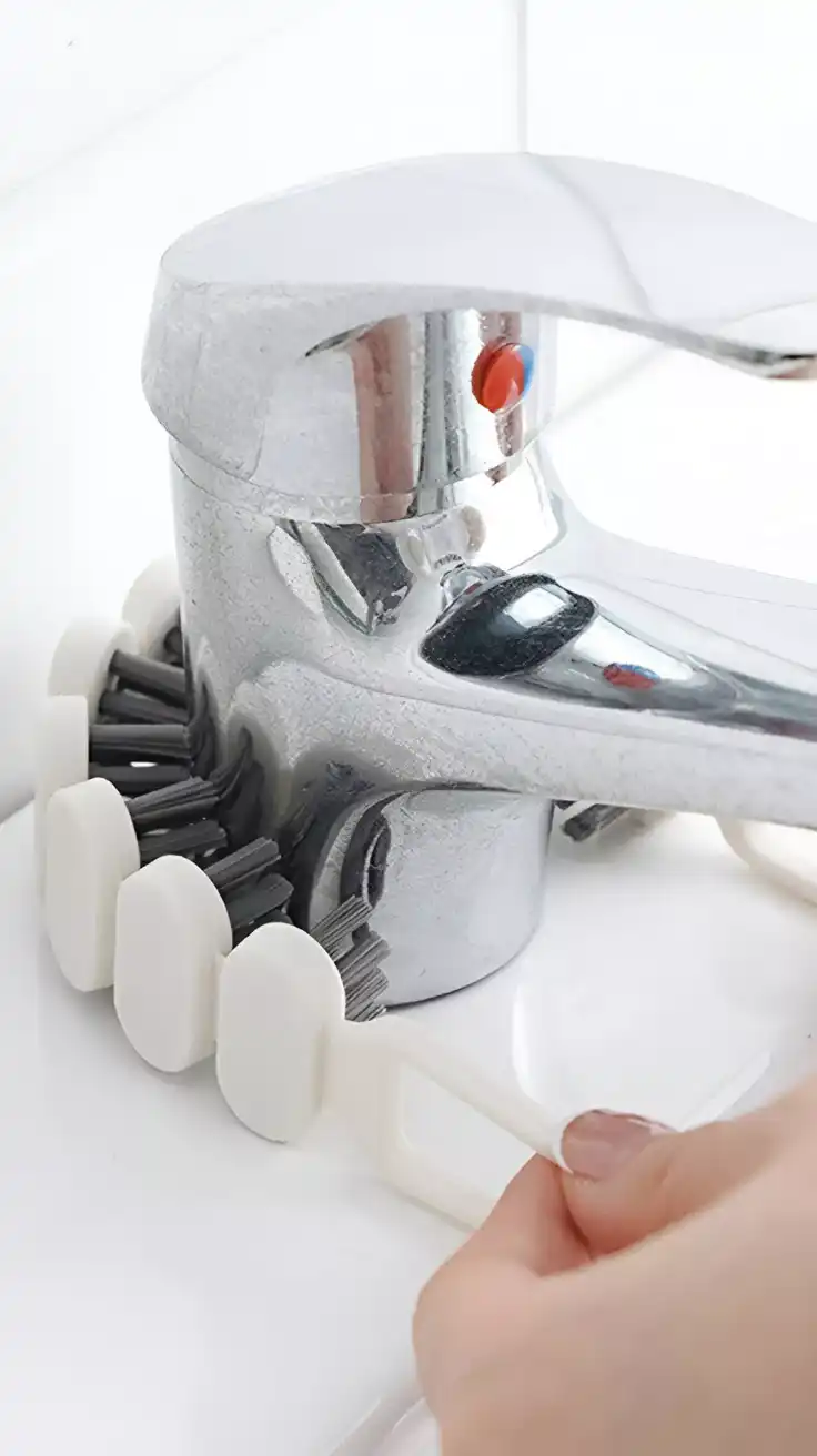 A bendable crevice cleaning brush reaching behind a faucet, a useful tool for kitchen cleaning hacks.